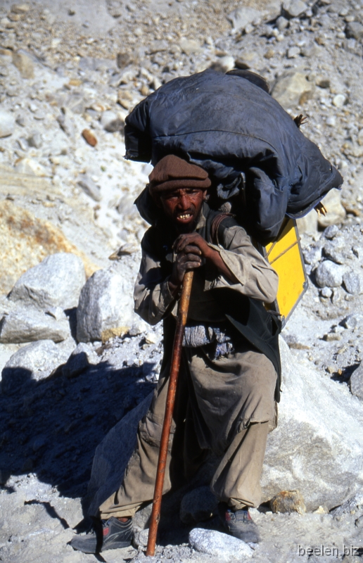 079_Baltoro Balti Porter Balti porter.
At this close a distance they smell strongly like sweat and fire-smoke.
I guess they wash hardly ever.
They walk without socks in plastic shoes, they carry their 25 kilo load plus their personal belongings mostly with a rope tied over their shoulders.
They still go real fast, but they have to pause frequently.